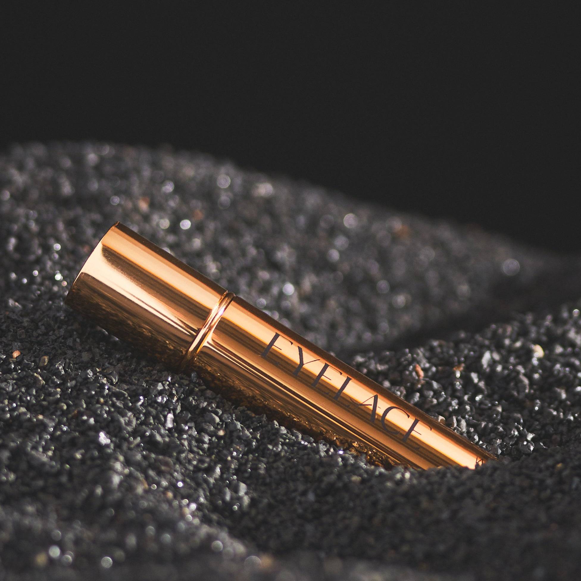 Eyelace White Lash Glue in gold tube on black sand